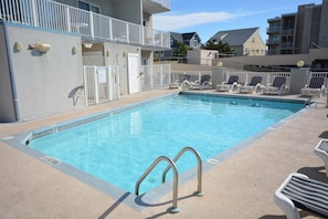 A swimming pool with lounge chairs and a building with balconies in the background.