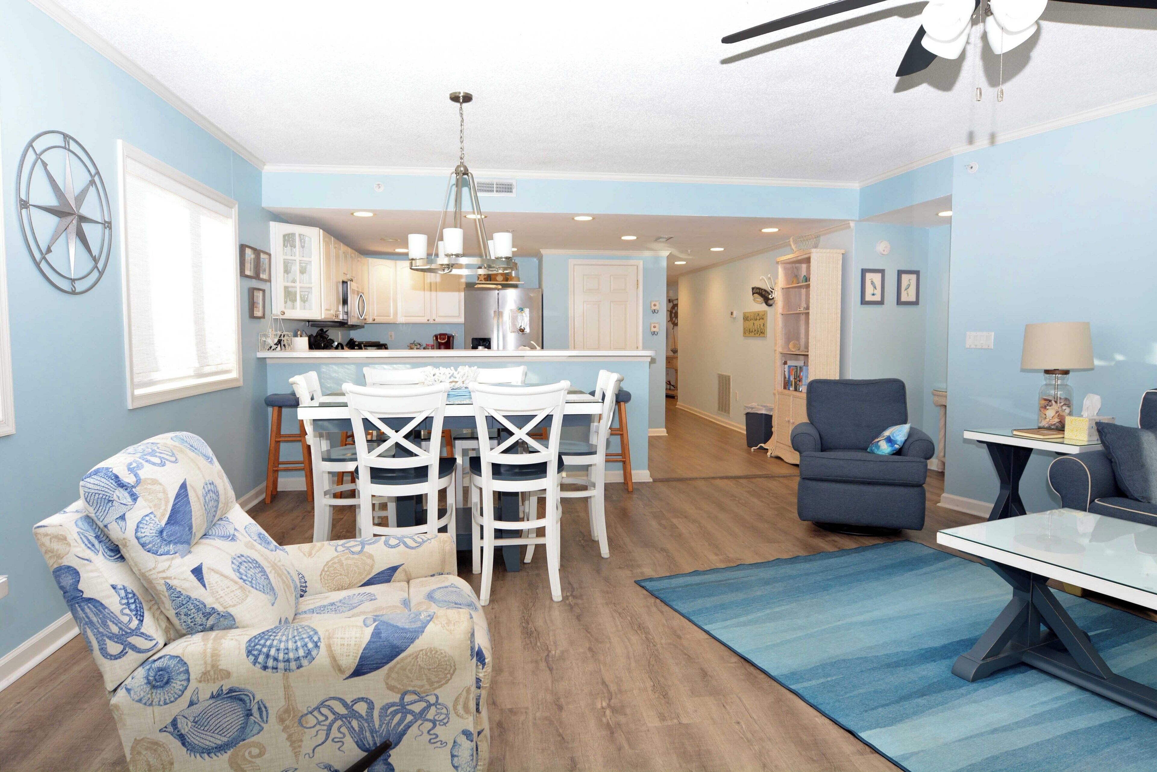 A dining area with a white table and chairs, a blue patterned sofa, and a ceiling fan.