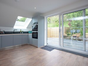 Een moderne keuken met een dakraam, grote schuifdeuren naar een terras en uitzicht op een tuin.