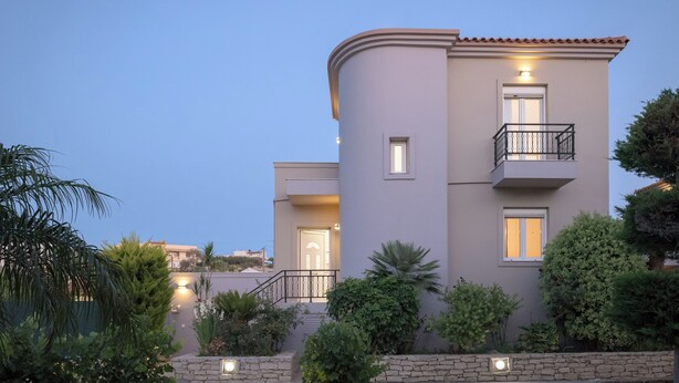 Une maison moderne à deux étages, dotée d’une façade incurvée, d’un balcon avec une balustrade et d’une entrée bien éclairée.