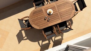 Une table en bois placée à l’extérieur, avec des chaises, un chapeau de soleil et deux verres posés sur la table.