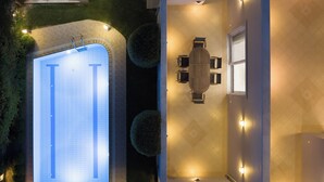 Vue aérienne d’une maison moderne dotée d’une piscine, d’un coin repas avec une table et des chaises, et d’une terrasse bien éclairée.