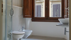 A bathroom with a glass shower enclosure, two sinks, and a wooden cabinet above a window. - Large private room in historycal building (Firenze)