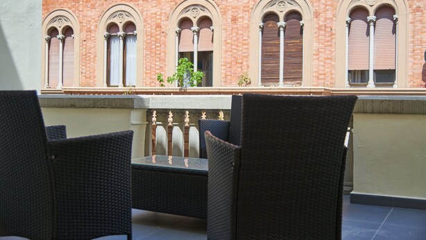 A terrace with wicker furniture and a brick building with arched windows in the background. - Large private room in historycal building (Firenze)