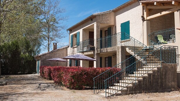 A two-story building with a balcony, a staircase, and outdoor seating with umbrellas.