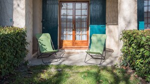 A covered porch with a wooden door, two green folding chairs, and a concrete floor.