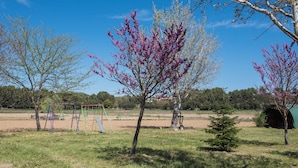 A park with playground equipment, trees, and a green structure in the background.
