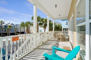 A covered outdoor area with a white railing, a pool, and a table with chairs. - 8BR Beach Oasis w/ Pool & Rooftop (Isle of Palms)
