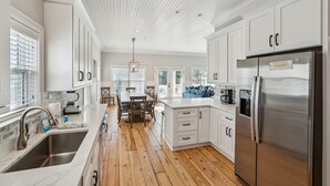 A modern kitchen with white cabinetry, a stainless steel refrigerator, and a wooden floor. - 8BR Beach Oasis w/ Pool & Rooftop (Isle of Palms)