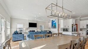 A spacious living area with a wooden dining table, blue sofa, and a ceiling fan. - 8BR Beach Oasis w/ Pool & Rooftop (Isle of Palms)