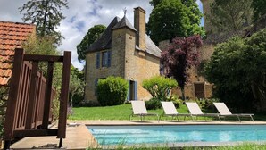 A stone building with a pool, lounge chairs, and a wooden deck.