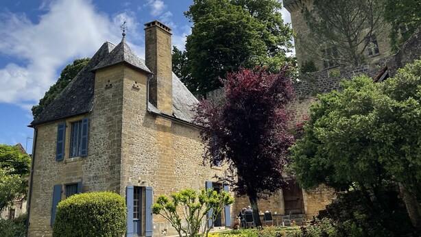 A stone building with a tower, surrounded by well-maintained gardens and a clear blue sky.