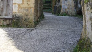 A narrow cobblestone street flanked by stone buildings with traditional architecture, including a wooden door and a stone wall with a window.