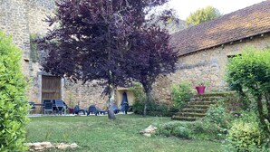 A stone building with a grassy courtyard, outdoor seating, and a tree.