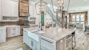 A spacious kitchen with a large island, modern appliances, and a rustic wooden accent wall. - Luxury Home 1 Minute to the Gulf, with LSV, Bikes, and Heated Pool (Santa Rosa Beach)