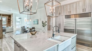 A modern kitchen with a large island, stainless steel appliances, and a unique geometric chandelier. - Luxury Home 1 Minute to the Gulf, with LSV, Bikes, and Heated Pool (Santa Rosa Beach)