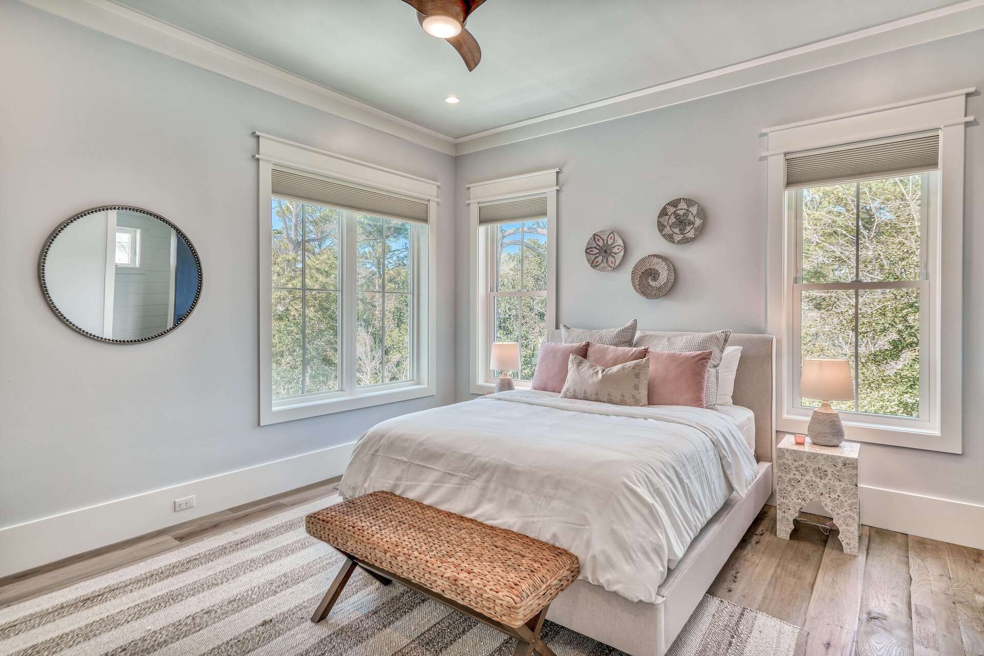 A bedroom with a large bed, two bedside tables, a bench, and a ceiling fan.