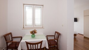 Un coin repas avec une table et des chaises, une fenêtre avec des stores et un lit à l’arrière-plan.