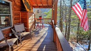 Eine Holzhütte mit Veranda, zwei Stühlen, einem Tisch und einer amerikanischen Flagge.