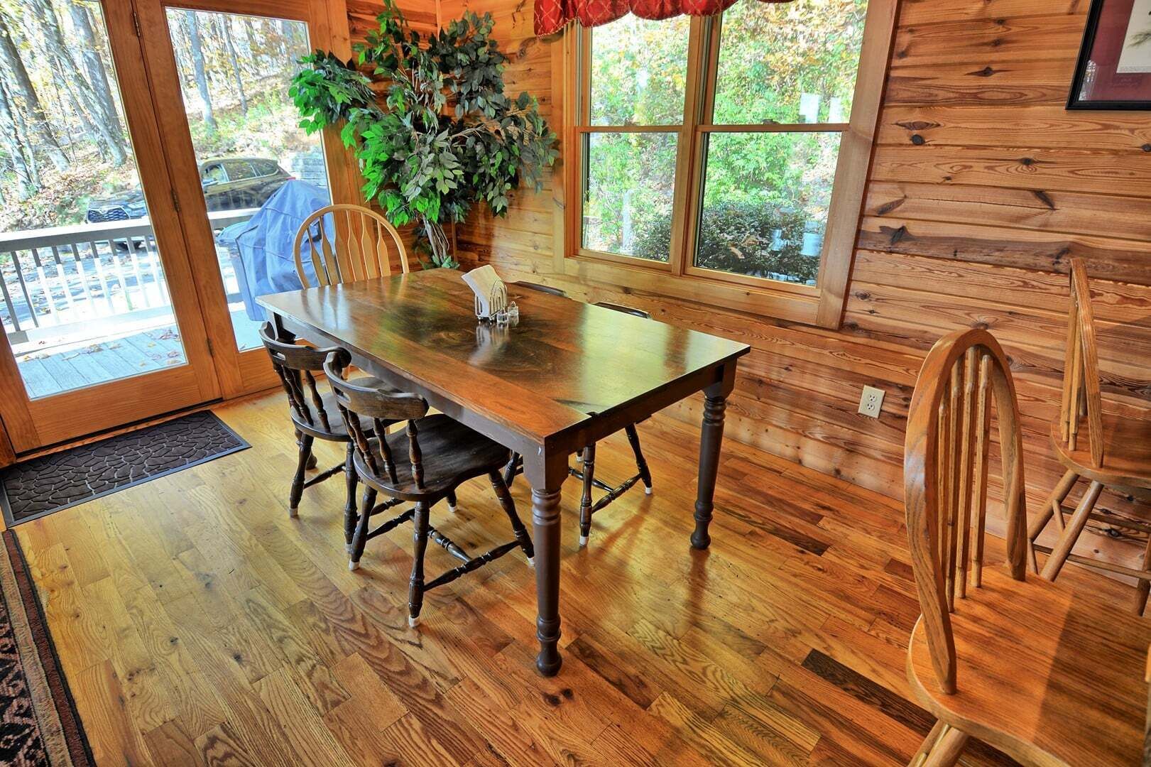 A wooden dining table with chairs, a potted plant, and a window with a view of trees.