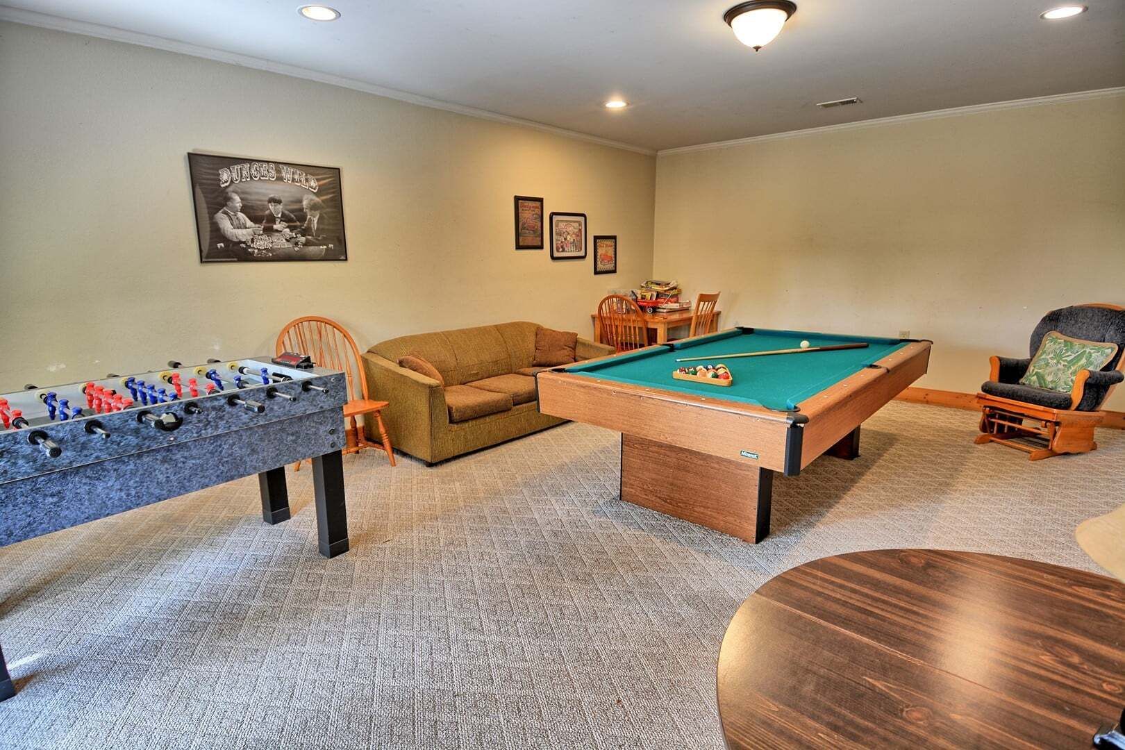 A room with a foosball table, a pool table, a sofa, and a chair.