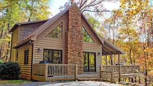 A log cabin with a stone chimney, large windows, and a porch with railings. - Spacious 3-bedroom cabin in West Jefferson, NC with game room and cozy fireplace. (West Jefferson)