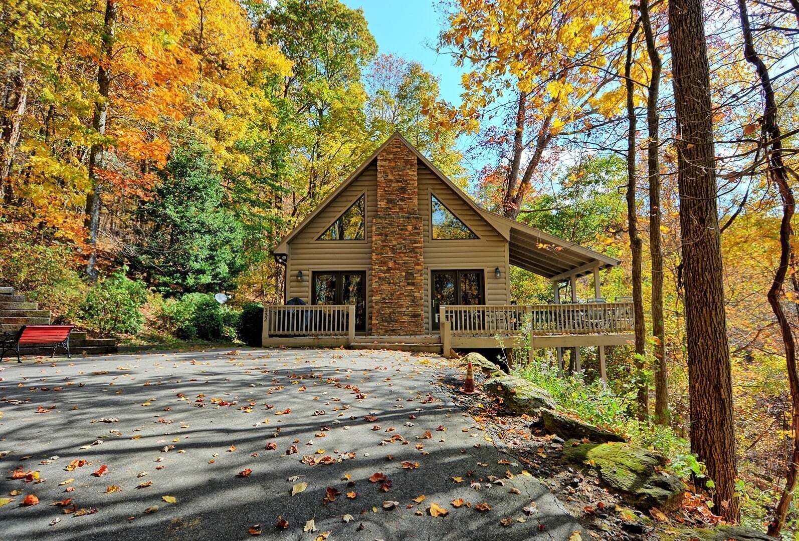 Une cabane à la façade en pierre, dotée d’un porche et d’une allée bordée de feuilles éparses.