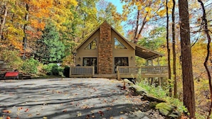 A cabin with a stone facade, a porch, and a driveway with scattered leaves. - Spacious 3-bedroom cabin in West Jefferson, NC with game room and cozy fireplace. (West Jefferson)