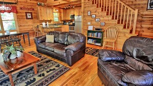 A wooden cabin interior with a living room, kitchen, and staircase. - Spacious 3-bedroom cabin in West Jefferson, NC with game room and cozy fireplace. (West Jefferson)