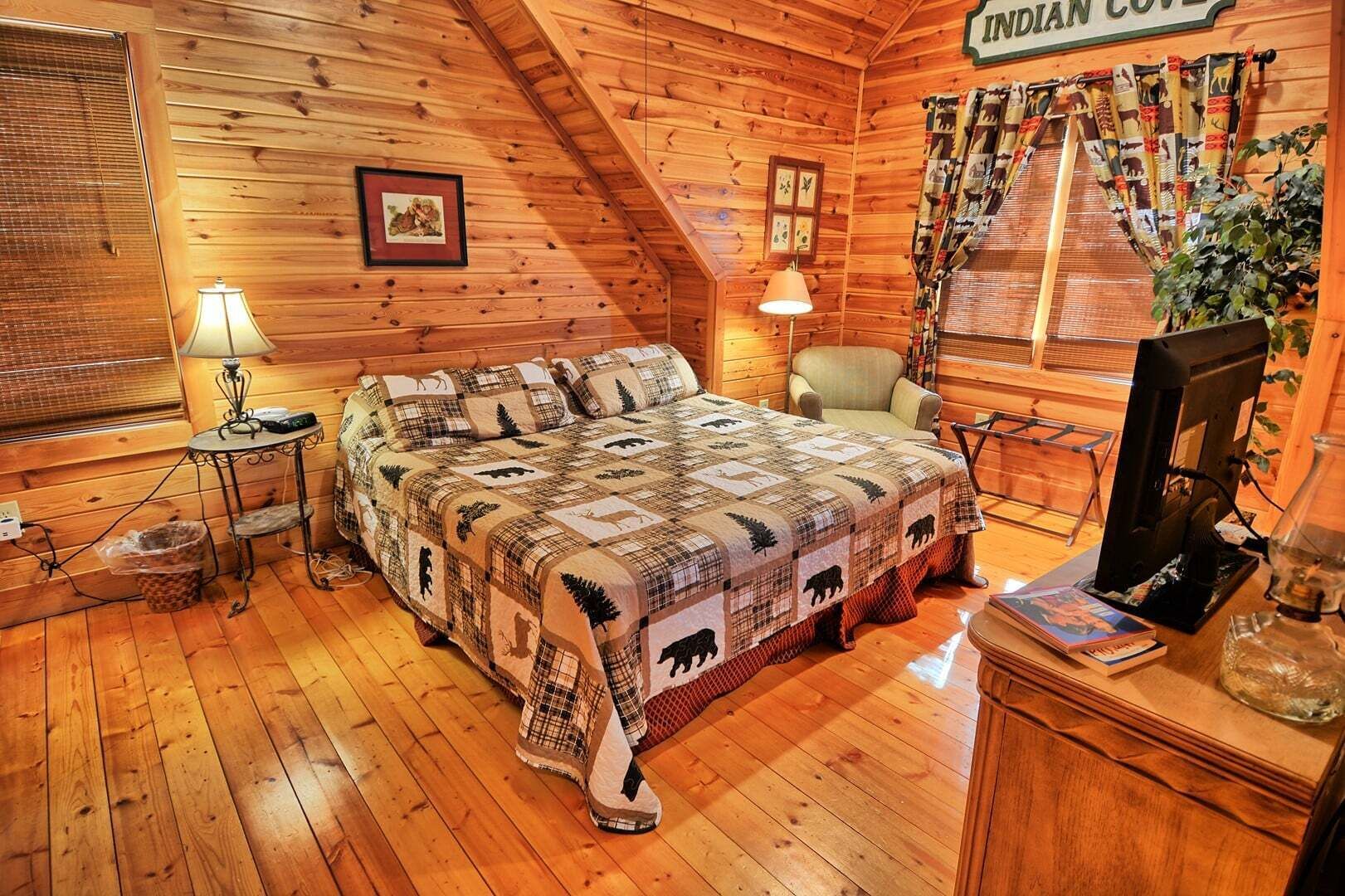 Une chambre aménagée dans un chalet en rondins, avec un lit, une chaise, un bureau avec un ordinateur et une fenêtre avec des rideaux.