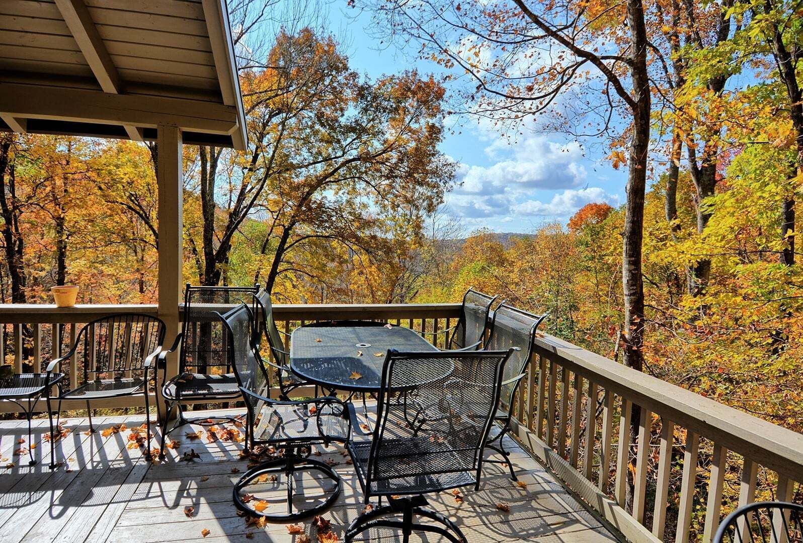 A covered outdoor deck with a table and chairs, surrounded by autumn foliage.