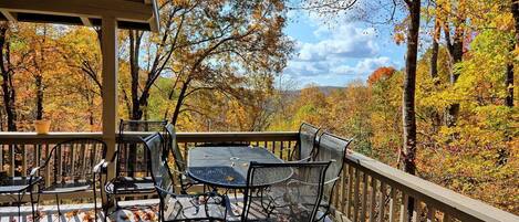A covered outdoor deck with a table and chairs, surrounded by autumn foliage.