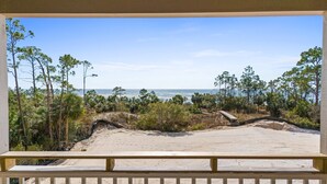 A beach view from a balcony with a wooden railing, sandy beach, and dense trees in the background. - Redbird Beach: 7BR Beachfront Home- Priv. Pool, Pet Friendly, Sleeps 23! (Port St Joe)