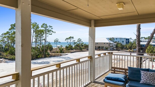 A covered balcony with a view of the beach and ocean, wooden furniture, and a clear sky. - Redbird Beach: 7BR Beachfront Home- Priv. Pool, Pet Friendly, Sleeps 23! (Port St Joe)