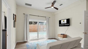 A modern living room with a sofa, a flat-screen TV, and a ceiling fan. - Redbird Beach: 7BR Beachfront Home- Priv. Pool, Pet Friendly, Sleeps 23! (Port St Joe)