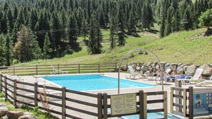 Una piscina con cerramiento de madera, rodeada por un muro de piedra y un cartel.