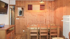 Una habitación con paneles de madera, una mesa y sillas de madera, un televisor y un refrigerador.
