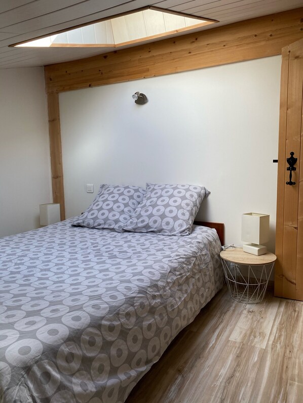 A bedroom with a bed, a bedside table with a lamp, a wooden wardrobe, and a skylight. - "Le Chai" 3 Stars (Gensac-la-Pallue)