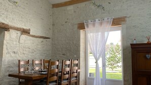 En matplats med ett träbord och stolar, ett fönster med en tunn gardin och utsikt över grönskan utanför.