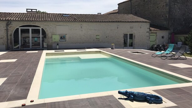 En swimmingpool med ett kaklat poolområde, solstolar och en byggnad med ett kaklat tak i bakgrunden.