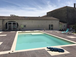 A swimming pool with a tiled deck, lounge chairs, and a building with a tiled roof in the background. - "Le Chai" 3 Stars (Gensac-la-Pallue)