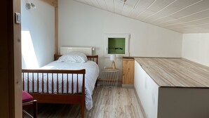 Ett sovrum med en säng, en trästol, ett litet bord med en lampa och ett skåp.