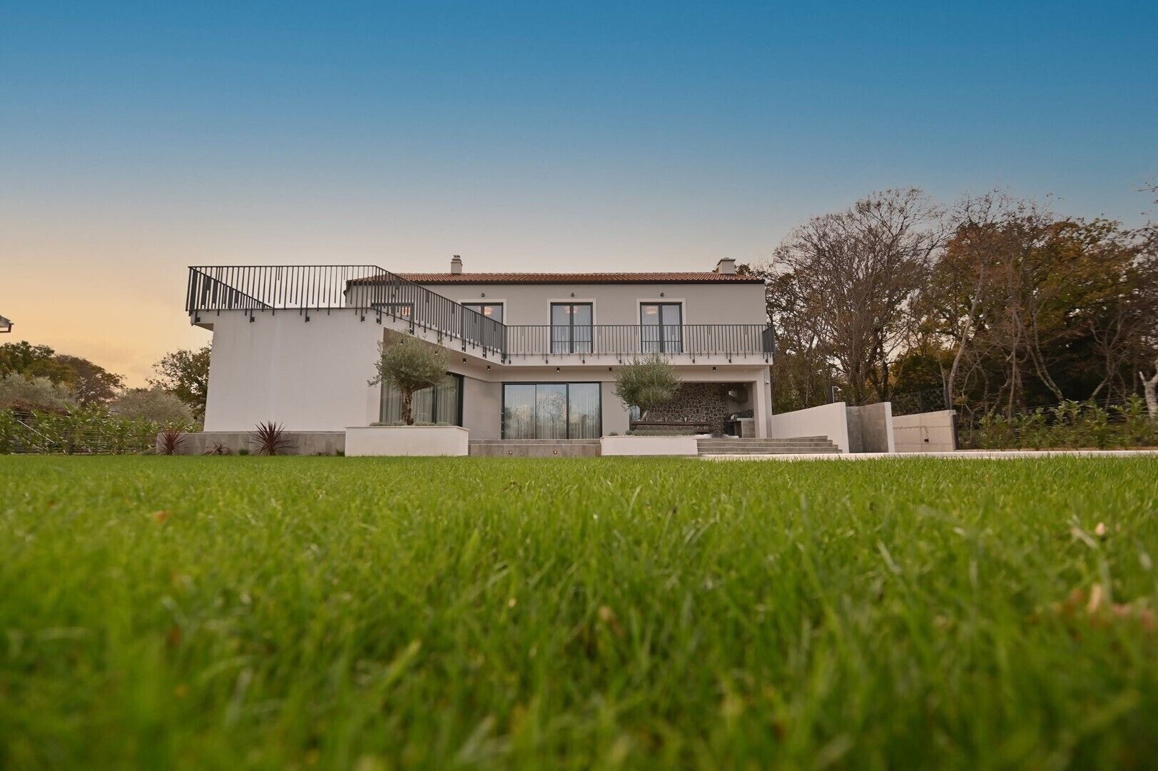 A modern two-story house with a balcony, a stone facade, and a well-maintained lawn.