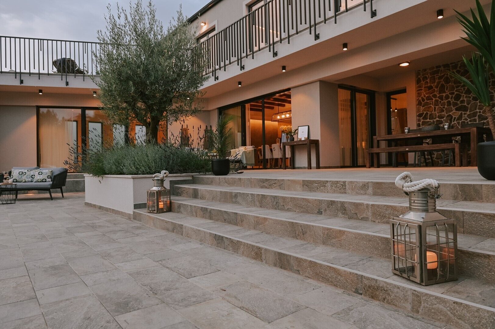 Un edificio moderno con fachada de piedra, zona de estar al aire libre y escalones que conducen a una entrada.