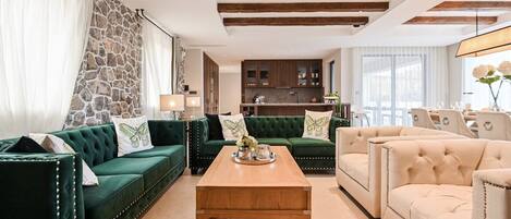 A living room with a green sofa, a beige sofa, and a wooden coffee table. There is a stone wall and a wooden ceiling beam.