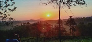 A sunset over a hilly landscape with trees and a person taking a photo. - Ripon Heritage Bungalow (Vythiri)