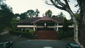 A two-story building with a red and white facade, a central staircase, and a small porch area. - Ripon Heritage Bungalow (Vythiri)