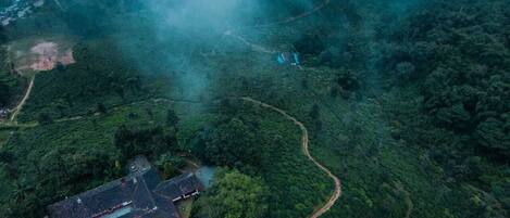An aerial view of a rural area with a winding road, a small building, and dense forest.