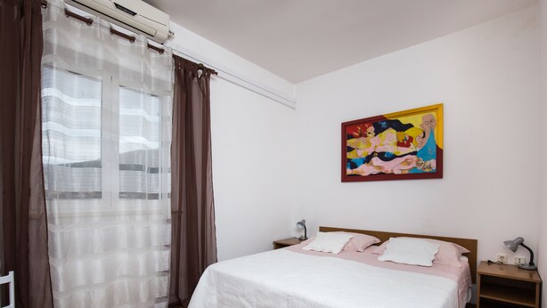 A bedroom with a bed, a nightstand, a wall-mounted painting, and a window with curtains. - Villa Konalić - Double or Twin Room with Balcony and Sea View 1 (Mokosica)
