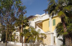 Un edificio moderno con facciata gialla, balconi bianchi e palme.